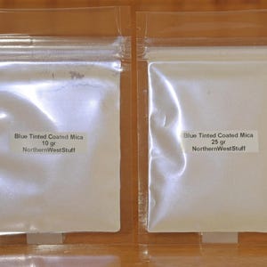 May include: Two clear plastic bags containing blue-tinted coated mica powder. The bags are labeled with the text "Blue Tinted Coated Mica" and "NorthernWestStuff". One bag contains 10 grams, the other 25 grams.