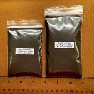 May include: Two clear plastic bags filled with black iron oxide fine magnetite. The bags are sealed and labeled with product information, including the weight in grams. A ruler is placed below the bags.