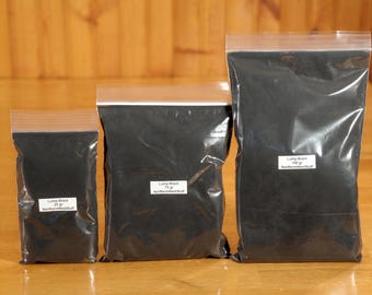 May include: Three sealed plastic bags filled with black powder, labeled "Lamp Black" with varying weights: 25g, 75g, and 100g. The bags are arranged on a wooden surface, with the labels indicating the product and the seller.