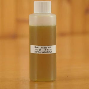 May include: A clear plastic bottle filled with raw linseed oil. The oil has a yellowish-green hue. A white label on the bottle reads "Raw Linseed Oil 100 gr (~4 fl oz) NorthernWestStuff". The bottle has a white cap.