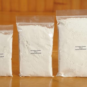 May include: Three clear plastic bags filled with white pottery plaster. The bags are labeled with the weight of the plaster in grams and the text "#1 Pottery Plaster NorthernWestStuff". The bags are arranged from smallest to largest.