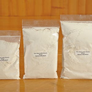 May include: Three clear plastic bags filled with white powder, labeled "Kiln Wash (with Zircon)" and varying weights: 100g, 200g, and 400g. The bags are sealed and sit on a wooden surface.