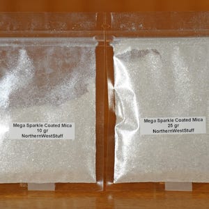 May include: Two clear plastic bags filled with white, glittery powder. Each bag has a white label with black text that reads "Mega Sparkle Coated Mica" and "NorthernWestStuff". One bag contains 10 grams, the other 25 grams.