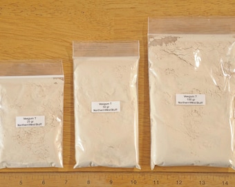 Może przedstawiać: Trzy przezroczyste plastikowe torebki wypełnione jasno-beżowym proszkiem, oznaczone wagą 25 g, 50 g i 100 g. Torebki są zamknięte i umieszczone na drewnianej powierzchni. Etykiety zawierają napisy "Veegum T" i "Northern West Stuff."