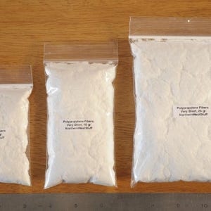May include: Three clear plastic bags filled with white polypropylene fibers. The bags are sealed and labeled with the weight of the fibers in grams. A ruler is at the bottom of the image.