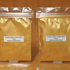 May include: Two clear plastic bags filled with yellow gold coated mica powder. The bags have white labels that read "Yellow Gold Coated Mica" and "NorthernWestStuff". One bag contains 10 grams, the other 25 grams.