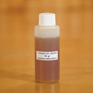 May include: A clear plastic bottle with a white cap, containing boiled linseed oil. The label reads "Linseed Oil, Boiled 50 gr NorthernWestStuff". The oil is a brownish color.