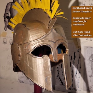 Puede incluir: Un casco griego de cartón de color dorado con una cresta de papel amarillo brillante. El casco presenta un protector nasal y aberturas para los ojos. El texto en la imagen dice: Cardboard Greek Helmet Template, handmade paper templates for cardboard, with links to full video instructions.