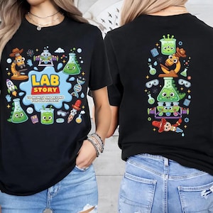 May include: Black t-shirt with a colorful cartoon graphic. The front features the text "LAB STORY" with lab-themed illustrations. The back of the shirt has a vertical arrangement of similar lab-themed cartoon graphics. The shirt is made of a soft material.