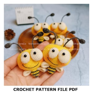 Può includere: Una collezione di giocattoli a forma di ape all'uncinetto gialli e bianchi con antenne nere e facce sorridenti. Le api hanno addomi a strisce nere e gialle e piccole ali bianche. Il testo "CROCHET PATTERN FILE PDF" è in basso.