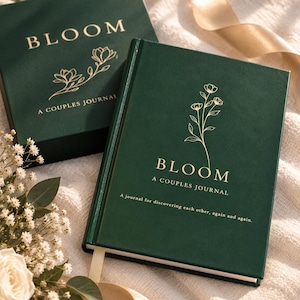 May include: A dark green hardcover journal titled BLOOM A COUPLES JOURNAL with gold foil floral illustrations and text. The cover features the phrase A journal for discovering each other, again and again. A matching green box is positioned behind the journal.