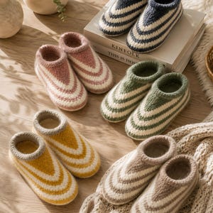 Puede incluir: Cinco pares de zapatillas de punto hasta el tobillo en varios colores, incluyendo azul marino, rosa empolvado, verde salvia, amarillo mostaza y beige. Cada par presenta un patrón de rayas en chevrón con detalles blancos y un puño acanalado.
