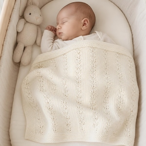 May include: A sleeping baby is nestled in a wooden bassinet, covered with a cream-colored knitted blanket. A stuffed bunny toy rests beside the baby. The blanket features a repeating leaf pattern.