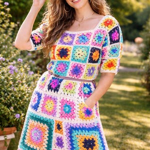 May include: A colorful crochet dress with a square pattern in various colors, including pink, blue, yellow, and green. The dress has short sleeves, a square neckline, and a matching belt. A straw hat completes the look.