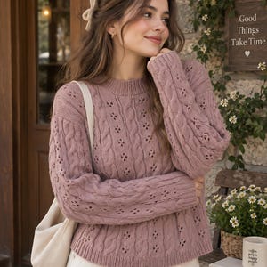 Può includere: Un maglione a maniche lunghe color rosa polvere caratterizzato da un motivo a trecce intrecciato con delicati dettagli in pizzo traforato. Il capo presenta un girocollo a coste, polsini a coste e un orlo a coste in maglia.