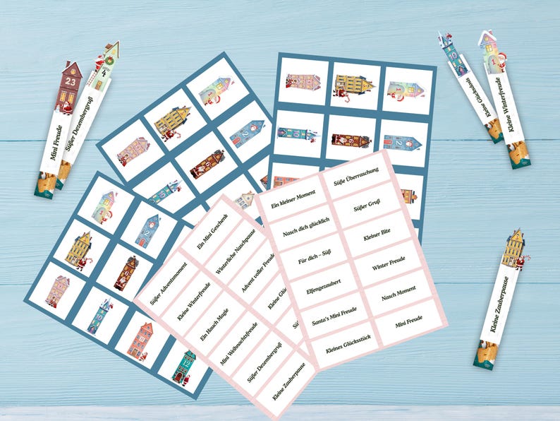 May include: A collection of Christmas-themed paper goods, including cards with house illustrations and labels with German text. The cards are arranged on a light blue surface. The image includes decorative bookmarks with house designs and the text "Mini Freude" and "S&uuml;&szlig;er Dezembergru&szlig;".