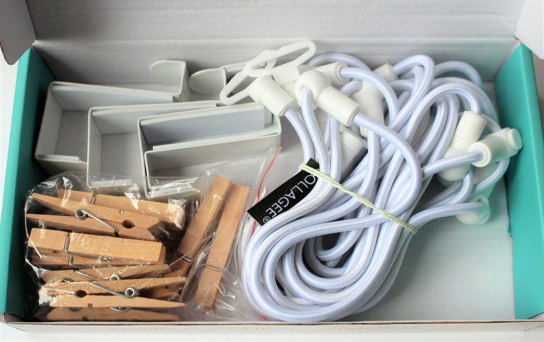 May include: A white box containing a set of white plastic picture hanging clips, white elastic cord, and wooden clothespins. The box also includes a label that says "OULAGEE".