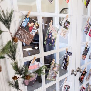 May include: A white door with a glass pane is decorated with holiday cards. The cards are hung on a white string with clothespins. The cards feature various holiday greetings and images of families.
