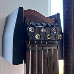 May include: A black guitar headstock and fretboard mounted on a wall. The guitar has six strings and a dark wood fretboard. The headstock is black with silver hardware. The wall mount is black.