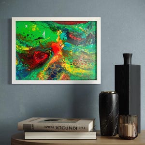 Può includere: Dipinto di arte astratta in una cornice bianca, con un vivace mix di colori verdi, rossi, gialli e blu. L'opera d'arte è esposta su una parete sopra un tavolo di legno con oggetti decorativi, tra cui libri, vasi e un portacandele.