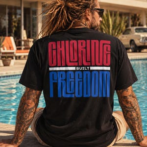 Könnte beinhalten: Ein schwarzes Kurzarm-T-Shirt mit einem Grafikdruck auf der Rückseite, der den roten Schriftzug CHLORINE über einer weißen horizontalen Linie und dem Wort BUILT sowie dem blauen Schriftzug FREEDOM zeigt. Das Design nutzt eine fette, serifenlose Schrift.