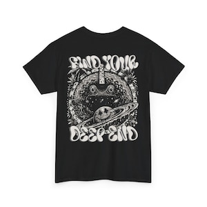 Könnte beinhalten: Ein schwarzes Kurzarm-T-Shirt mit einem weißen Grafikdruck auf der Rückseite. Das Design zeigt einen Frosch in einer kreisförmigen Weltraumszene mit einem Planeten mit Smiley-Gesicht und Ringen. Der Text "FIND YOUR DEEP END" ist in Fettschrift gedruckt.