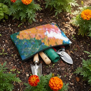 May include: A zipped pouch with a floral design, containing gardening tools. The pouch is open, revealing a trowel, twine, and pruning shears. The scene is set in a garden with orange marigold flowers and dark soil.