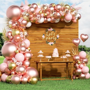 May include: A party scene with a wooden backdrop, adorned with a balloon arch in shades of pink, gold, and clear. A table displays a cake and desserts. Heart-shaped balloons float nearby, and the text "Let's party" is visible.