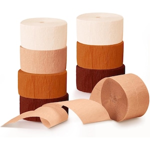 May include: Several rolls of crepe paper in shades of cream, peach, orange, and burgundy are stacked. One roll is unraveled, showing the paper's texture. These are ideal for party decorations and craft projects.