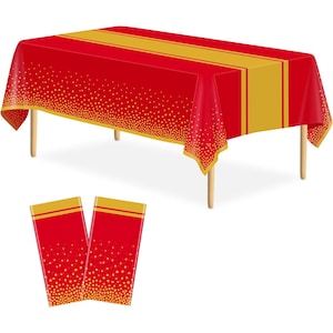 May include: A red rectangular tablecloth with a gold stripe down the center and gold polka dots along the edges. Two matching red placemats with gold polka dots are also shown. The tablecloth is on a wooden table.