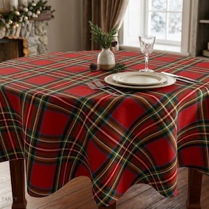 May include: A round tablecloth featuring a red, green, and white plaid pattern draped over a wooden table. The table is set with a white plate, a clear glass, a fork, and a knife. A small white vase with green sprigs sits in the center.