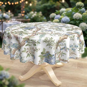 May include: A round tablecloth featuring a white background with a blue and brown botanical print of birds, branches, and flowers. The fabric drapes over a pedestal table, and the text TOP JOY PARTY is printed on the left side of the cloth.