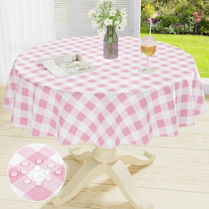 May include: A round table covered with a pink and white checkered tablecloth. On the table sits a clear glass vase containing white flowers with green stems and a clear glass filled with a golden liquid. A small circular inset shows the fabric texture.