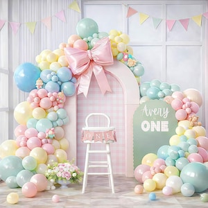 May include: A pastel-colored balloon arch with a large pink bow, surrounding a white high chair. The backdrop includes a sign that says "Avery is ONE". The scene is decorated with pastel balloons, flowers, and a banner that says "ONE".