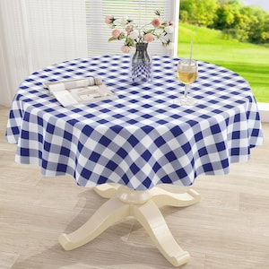 May include: A round table with a blue and white checkered tablecloth, featuring a glass vase filled with pink and white flowers, an open book, and a clear glass of amber liquid, supported by a white pedestal base on a light wood floor.