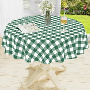 May include: A round table covered with a green and white checkered tablecloth. On the table sits a clear glass vase containing white flowers, a white open book, and a clear glass filled with a light-colored liquid on a pedestal base.