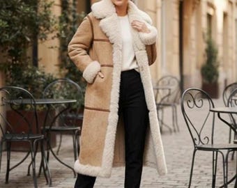 Peut inclure: Un long manteau en peau de mouton beige avec une garniture et une doublure en peau de mouton crème. Le manteau a un large col et est porté sur un pull blanc et un pantalon noir. Le cadre est un café en plein air.