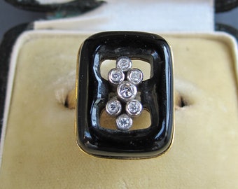 May include: A black and gold ring with a rectangular black enamel setting and a cluster of diamonds in the center. The ring is in a black velvet ring box.