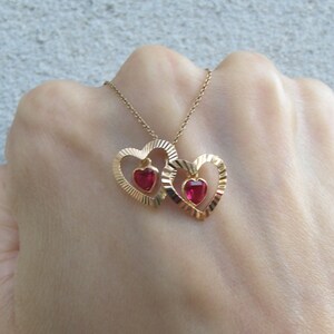 May include: A gold necklace with two interlocking heart pendants, each featuring a red gemstone in the center.