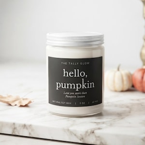 Può includere: Una candela in barattolo di vetro trasparente con coperchio bianco ed etichetta nera. L'etichetta riporta THE TALLY GLOW, hello, pumpkin, Love you more than Pumpkin Season, NATURAL SOY WAX, 255g, 60 HRS. La candela contiene cera bianca cilindrica.