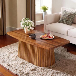 May include: A wooden coffee table with a ribbed base, displaying a natural wood grain. The table is set on a beige rug, with a white sofa and a patterned cushion in the background. A vase of white flowers, a bowl of dark berries, and a plate of food are on the table.