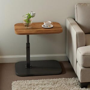 May include: A wooden side table with a dark metal base and adjustable height. The tabletop holds a cup of coffee on a saucer and a glass vase with flowers. The table is next to a beige sofa.