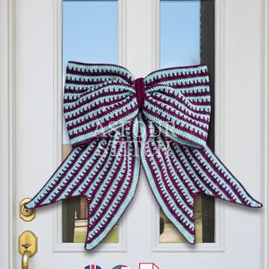 May include: A large, handmade crochet bow in shades of burgundy and light blue, displayed on a white door. The bow features a striped pattern and is designed for decorative purposes. The bow is a festive accent for the home.