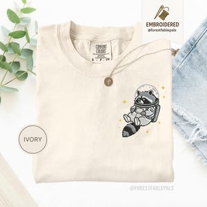 宇宙アライグマTシャツ、刺繍入りおもしろアライグマシャツ、かわいい宇宙動物Tシャツ、コンフォートカラーシャツ、アライグマ好きへのギフト、かわいい動物シャツ Ivory