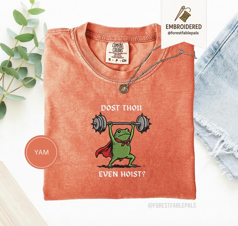 May include: Orange Comfort Colors t-shirt featuring a green frog lifting weights, wearing a red cape and a bow tie. The text "DOST THOU EVEN HOIST?" is above and below the frog. A silver necklace is on the shirt.