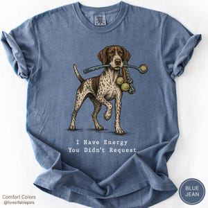 Könnte beinhalten: Ein blaues Kurzarm-T-Shirt mit einer Grafik eines braun-weiß gefleckten Hundes, der einen Ballwerfer und Tennisbälle im Maul hält. Der Text "I Have Energy You Didn't Request" ist in Weiß unter der Hundeillustration aufgedruckt.