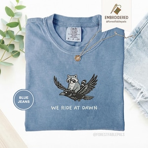 Vi rider i gryningen T-shirt, rolig tvättbjörn och kråka Korp T-shirt, broderade komfortfärger 1717, kaotisk djurskjorta, nyckfull spelpresent