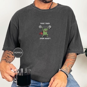 May include: Dark grey t-shirt with a cartoon frog lifting weights. The frog wears a red cape and bow tie, with the text "DOST THOU EVEN HOIST?" above and below the frog. The shirt has a Pepper brand label.