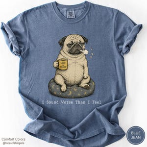 Könnte beinhalten: Ein blaues Kurzarm-T-Shirt mit einer Grafik eines Mopses, der auf einem Kissen sitzt und eine gelbe Tasse mit der Aufschrift LOUD & PROUD hält. Der Mops stößt eine Rauchwolke aus. Unter der Grafik steht der Text I Sound Worse Than I Feel.