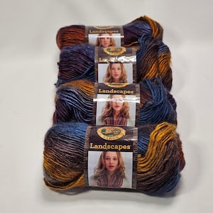 May include: Four skeins of Lion Brand Landscapes yarn stacked vertically. Each skein features a variegated color palette of deep blue, purple, and golden orange. A paper label wraps around the center of each, displaying the brand logo and text.